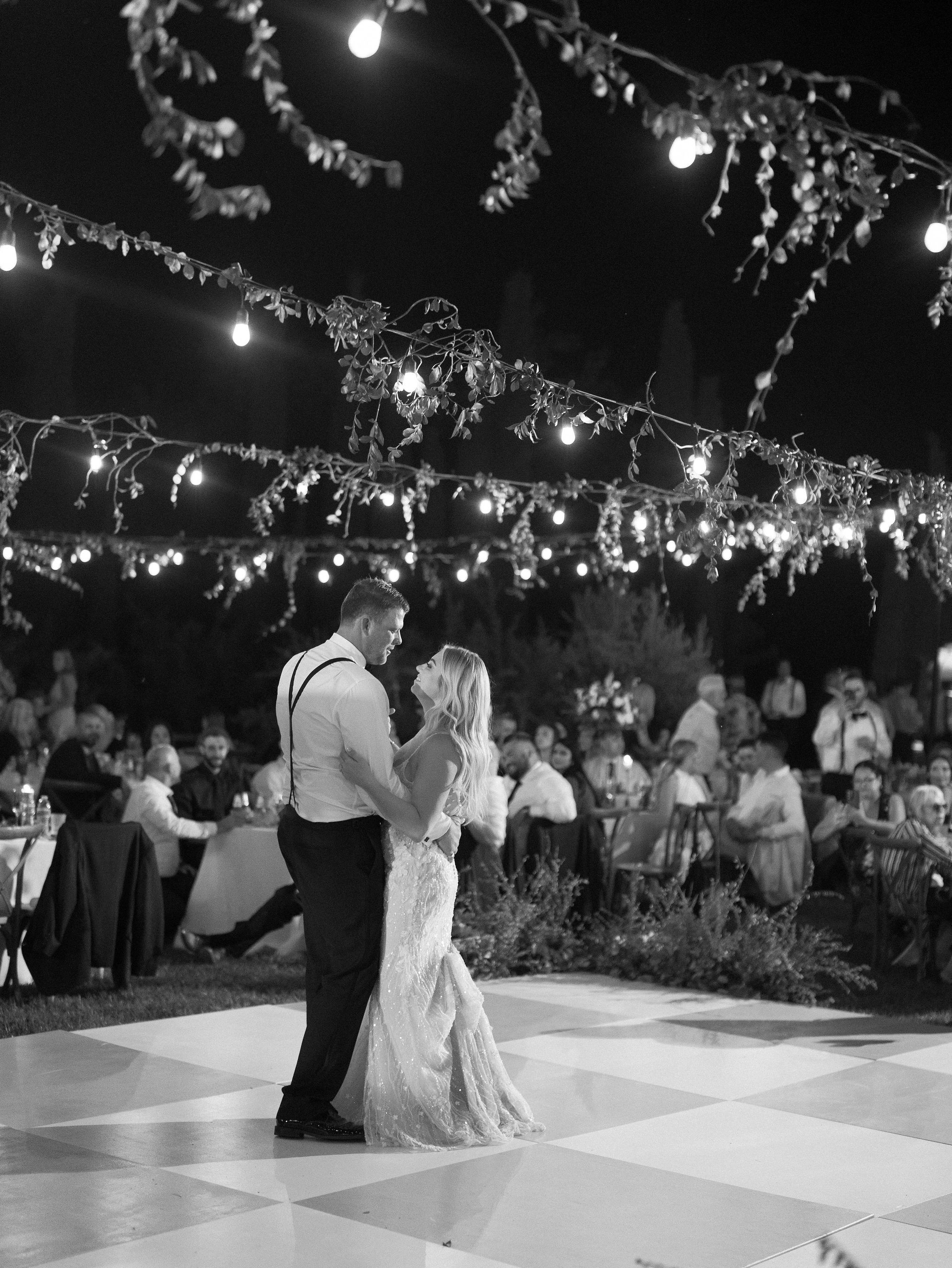A couple shares their first dance on a black and white checkered floor, framed by cold spark fountains